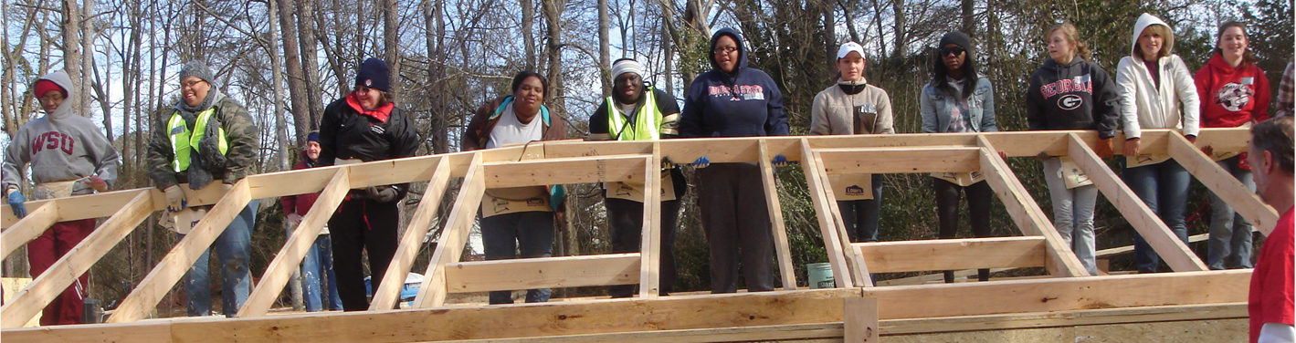 College-age volunteers raising the wood-framed wall of a house in winter