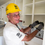 A volunteer attaches new doors to a kitchen cabinet