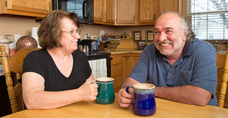 A middle-aged woman and man sitting at a kitchen table with cups of coffee