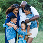 A family — mom, dad, two daughters, and a son — all dressed in blue and white smile and embrace outdoors
