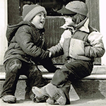 Two young children in cold-weather clothes shake hands while sitting on a stoop