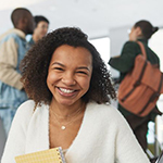 College age woman with notebook looking at the camera with other students in the background