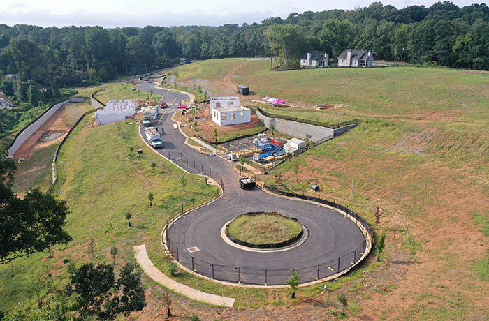 Aerial photo of a grassy field with a cul-de-sac road flanked by homes under construction with forest in the background